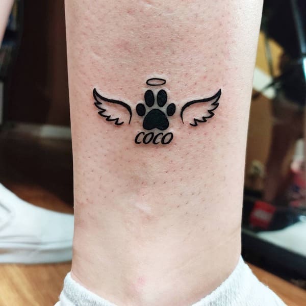 62 Beautiful Remembrance Tattoos for Dogs: A Heartfelt Tribute 35 Angel wings paw print memorial tattoo with name Coco and halo design on ankle